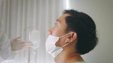 Pediatri elbisesi giymiş bir tıp çalışanı hastanede enfekte olmuş bir adamın ağzından alınan kovid 19 numunesi için test yapıyor.