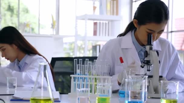 Genç Asyalı kadın bilim adamı laboratuarda laboratuvar önlüğü ve eldivenleriyle iş arkadaşıyla araştırma yapıyor. — Stok video