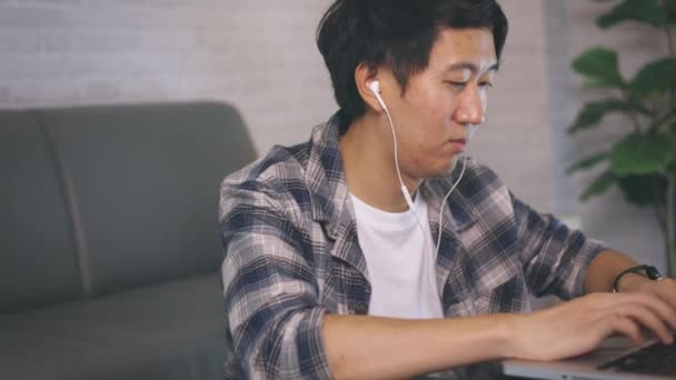 Jeune entrepreneur masculin asiatique dans le travail occasionnel et écouteur sur ordinateur portable à la fin de la nuit de la maison — Video