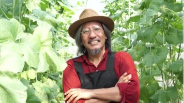 Yaşlı orta yaşlı erkek çiftçi kollarını kavuşturmuş mutlu diş tebessümüyle hasır şapka takıyor.