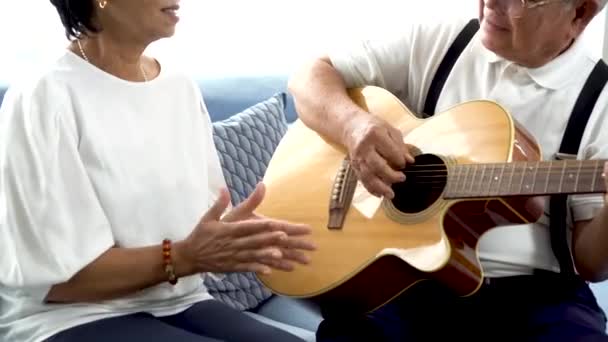 Asiática senior pareja sentado en el sofá y jugar acústica guitarra juntos en casa — Vídeo de stock
