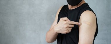 Aşılanmış genç adam Covid-19 aşısı olduktan sonra kollarını yapıştırıcı bandajla sargılıyor.