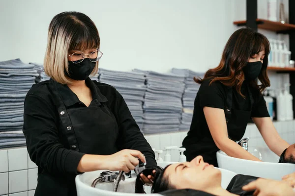 Hairdresser with mask washing customer hair