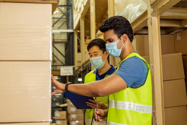 Group of young factory warehouse workers wearing a protective face mask while working in logistic industry. Asian and Indian ethnic men checking item stock order during Covid 19 pandemic — Stock Photo, Image