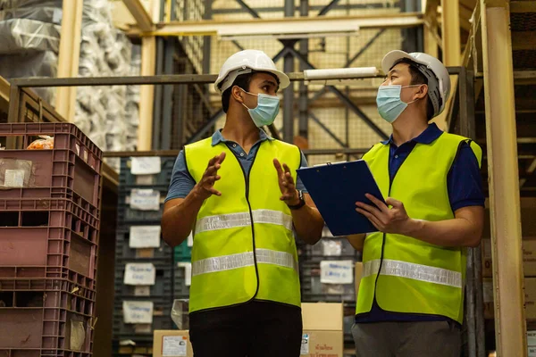 Group of young factory warehouse workers wearing a protective face mask while working in logistic industry. Asian and Indian ethnic men checking item stock order during Covid 19 pandemic — Stock Photo, Image