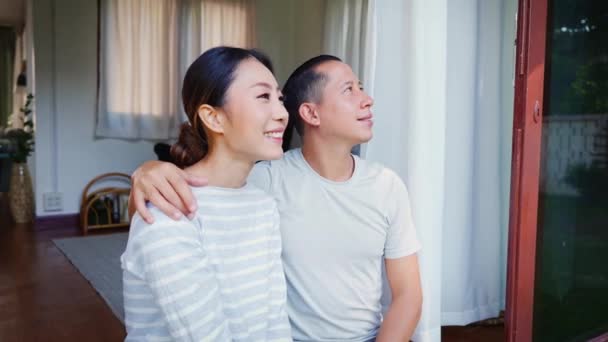Egy fiatal felnőtt ázsiai pár portréja, akik felnéznek, miközben egy férfi ujjal mutogat az otthoni belső háttérben. 30-as évekbeli sikeres férj és feleség. Ingatlan- és ingatlanfejlesztési koncepció — Stock videók