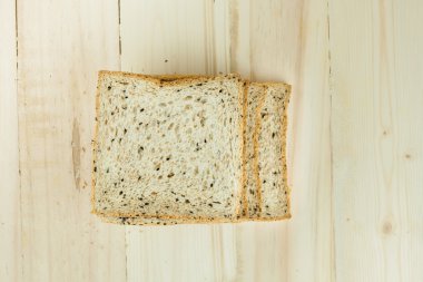 Taze dilim kepekli ekmek ile çeşitli tohum ve tahıllı ahşap arka plan siyah plaka üzerinde