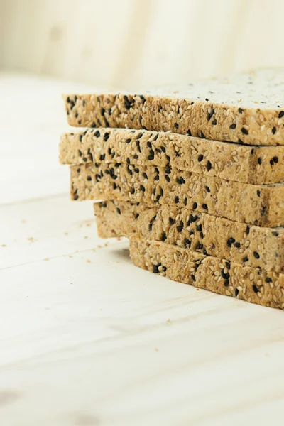 Fresh slices of wholewheat bread with various seeds and multigrain on the black plate in wood background — Stock Photo, Image
