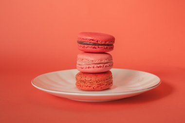 Pile of red-toned macaroons stacked up like a tower on white plate in red pastel isolated background