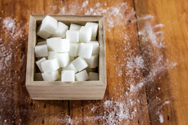 Sockerbitar i Square formad skål med oraffinerat socker spilla över i trä bakgrund — Stockfoto