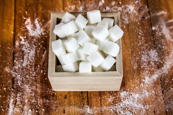 Sockerbitar i Square formad skål med oraffinerat socker spilla över i trä bakgrund — Stockfoto