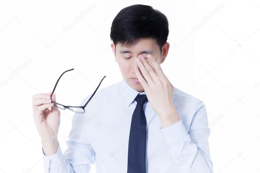 Young Asian businessman rubbing his tired eyes from long hours of works using computer