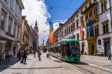 Graz, Avusturya - 19 Haziran 2020 - Modern tramvay treni Herrengasse alışveriş caddesinden geçiyor geleneksel Avusturya mimarisinin önünde insanlarla