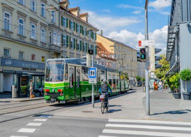Graz, Avusturya - 19 Haziran 2020 - Lendkai 'de eski tramvay treni, insanlar, bisikletçiler ve geleneksel Avusturya mimarisi ile sokak sahnesi