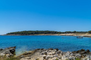 Kamenjak, Istria, Hırvatistan - 2 Temmuz 2020 - Taş plajda yüzücüler ve botlar