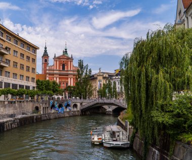 Ljubljana, Slovenya - 26 Haziran 2020 - arkasında güzel Fransisken kırmızı kilisesi olan Ljublanica nehrinde bir tekne