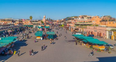 Marakeş, Fas - 14 Ocak 2021 - Jemaa el Fna Meydanı manzaralı insanlar, dükkanlar, portakal suyu tezgahları ve minareli cami