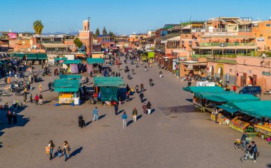 Marakeş, Fas - 14 Ocak 2021 - Jemaa el Fna Meydanı manzaralı insanlar, dükkanlar, portakal suyu tezgahları ve çatıdaki terastan bir minareyle cami