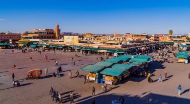 Marakeş, Fas - 14 Ocak 2021 - Jemaa el Fna Meydanı manzaralı insanlar, dükkanlar, portakal suyu tezgahları ve minareli cami