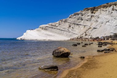 Realmonte, İtalya - 28 Temmuz 2020 - İtalya Realmonte, Sicilya 'daki Scala dei Turchi' nin beyaz kireçtaşı kayalıklarının önündeki kayalar ve kumsal manzarası