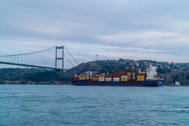 Bebek, İstanbul, Türkiye - 19 Şubat 2021 - İstanbul Boğazı 'nda Fatih Sultan Mehmet Köprüsü' nün altından geçen konteyner gemisi