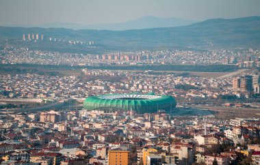 Bursa, Türkiye - 6 Mart 2021 - Bursa şehrinin arka planda Bursaspor Stadyumu ve dağları ile hava panoramik manzarası