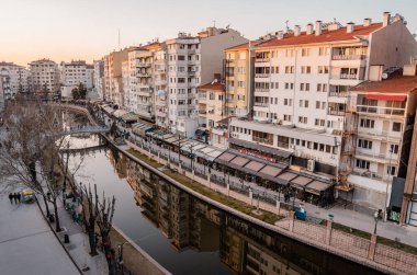Eskisehir, Türkiye - 8 Mart 2021 - Porsuk nehri üzerindeki binaların ve insanların panoramik günbatımı manzarası