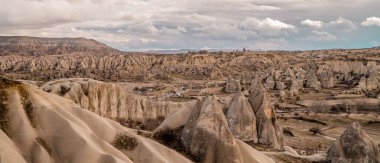 Bulutlu bir günde Türkiye 'nin Goreme kenti yakınlarında kaya oluşumları ve peri bacalarıyla eşsiz Kapadokya manzaralarının güzel yatay panoramik manzarası