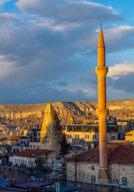 Goreme, Türkiye - 16 Mart 2021 - Tipik Kapadokya peri bacası içine inşa edilmiş otel ve restoranların dikey günbatımı manzarası