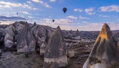 Goreme, Türkiye - 19 Mart 2021 - Cappadocia 'nın muhteşem manzaraları üzerinde uçan turist sıcak hava balonları ve tipik kaya oluşumlarının gündoğumu manzarası