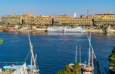 Aswan, Mısır - 2 Nisan 2021 - Nil Nehri üzerindeki Aswan şehrinin panoramik manzarası Nubian Köyü 'nden görülen yolcu gemisiyle