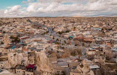 Goreme, Türkiye - 20 Mart 2021 - Türkiye 'nin Kapadokya kentindeki Goreme kasabasının yatay panoramik manzarası, peri bacaları, evleri, arabaları ve benzersiz kaya oluşumları