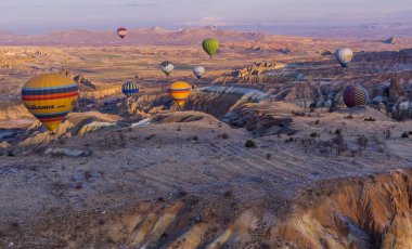 Urgup, Cappadocia, Türkiye - 19 Mart 2021 - Kapadokya 'daki muhteşem baca, kaya oluşumları ve dağlarla uçan sıcak hava balonlarının güzel panoramik hava manzarası