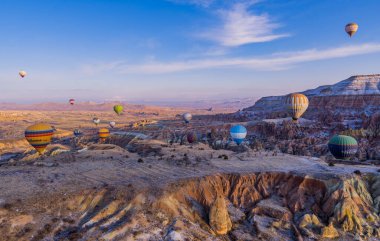 Urgup, Cappadocia, Türkiye - 19 Mart 2021 - Peri bacası, kaya oluşumları ve gün doğumunda Kapadokya 'da dağların üzerinde uçan sıcak hava balonları panorama hava manzarası