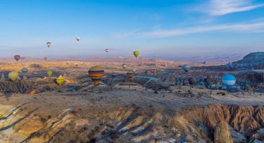 Urgup, Cappadocia, Türkiye - 19 Mart 2021 - Kapadokya 'daki muhteşem baca, kaya oluşumları ve dağların üzerinde uçan sıcak hava balonlarının güzel panoramik gündoğumu manzarası