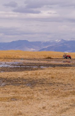 Türkiye 'nin orta kesimindeki Sultansazligi Milli Parkı' nda bulutlu bir günde gölün önündeki bir traktörün kasvetli dikey görüntüsü ve bataklıklar