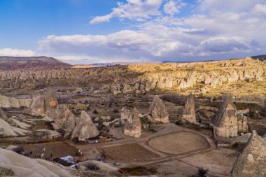 Goreme, Kapadokya, Türkiye 'deki eşsiz kaya oluşumlarına ve tipik peri bacalarına sahip bir at çiftliğinin panoramik günbatımı manzarası