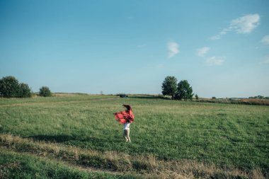 Kırmızı ekose yeşil tarla ve mavi gökyüzü arka planı tutan küçük çocuk.