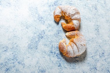 İki yeni pişmiş kruvasan ve mavi bir arka planda krema şekeri.