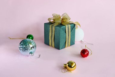 Pembe zemin üzerinde hediye kutusu ve renkli toplar.