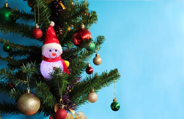 Suni Noel ağacında parlayan hafif kardan adam bebeği ve mavi arka planda izole edilmiş..