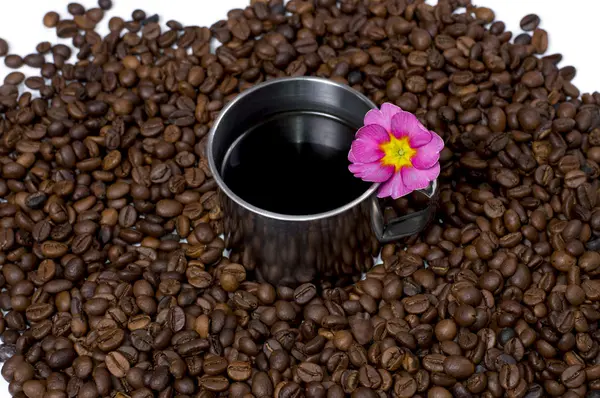 Steel cup of coffee in coffee grains and a flower — Stock Photo, Image