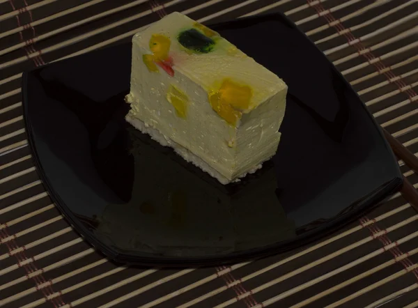 Gâteau jaune vif sur une assiette noire, sur un tapis brun — Photo