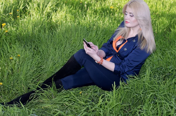 A bela menina em uma grama com telefone, uma grama verde — Fotografia de Stock