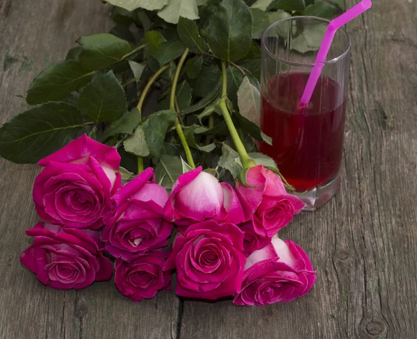 Bouquet of red roses and glass of juice with a tubule — Stock Photo, Image