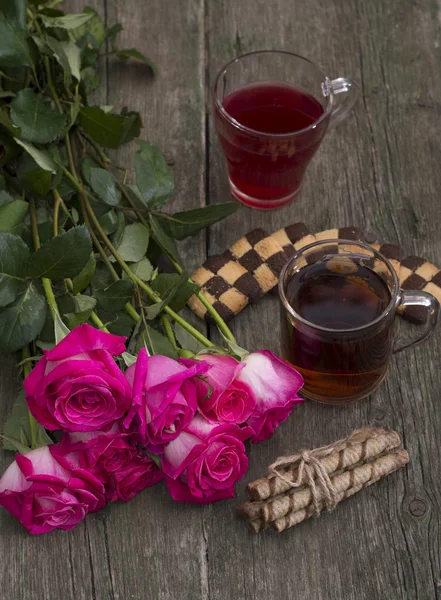 Два стакана напитка, печенье и букет алых красных роз — стоковое фото