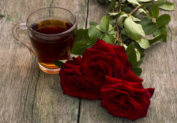 Чашка чаю і яскраво-червоні троянди на дерев'яному фоні — стокове фото
