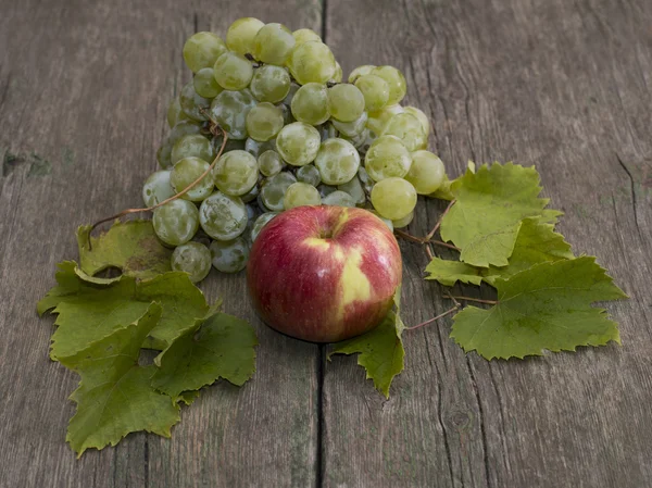 Manzana y racimo de uvas con hojas sobre una mesa de madera —  Fotos de Stock