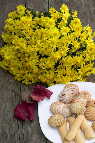 Букет желтых цветов, красный лист и тарелка с печеньем, на — стоковое фото