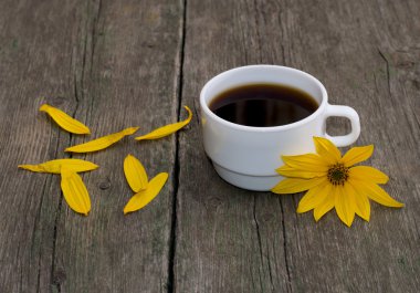 still life a white cup of coffee, a yellow flower and petals